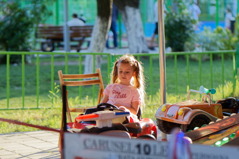 coming_soon_19 - Scene at a carousel where a child is riding a brightly colored amusement car